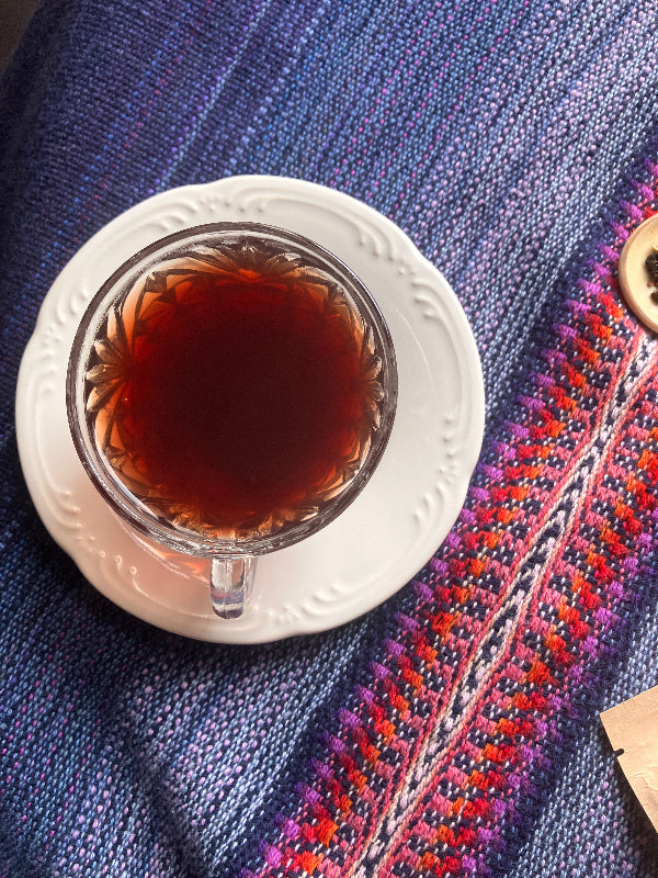 Teacup with dark liquid on a white saucer against a blue fabric background