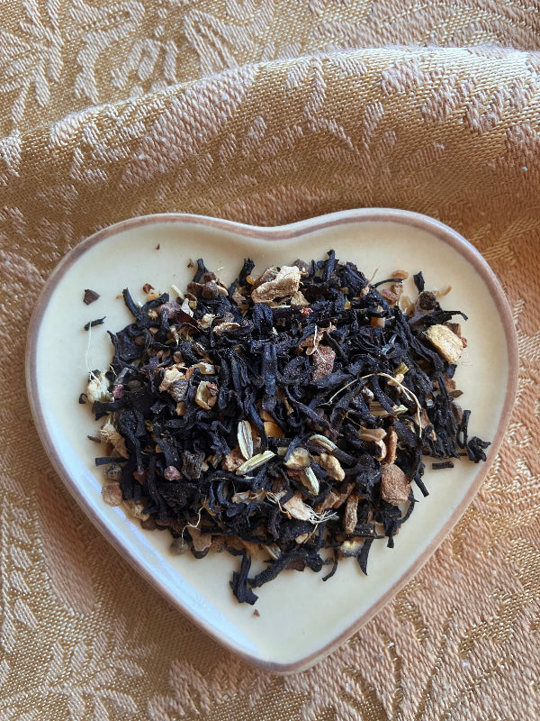 Dry black tea leaves on a white ceramic dish with a textured gold background