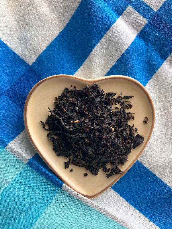Dried black tea leaves in a beige bowl on a blue and white checkered tablecloth