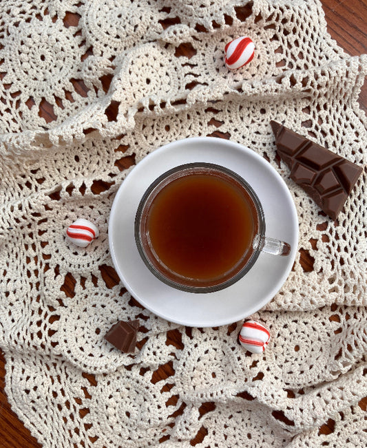 Tea cup with a crocheted doily, chocolate, and candies on a wooden surface