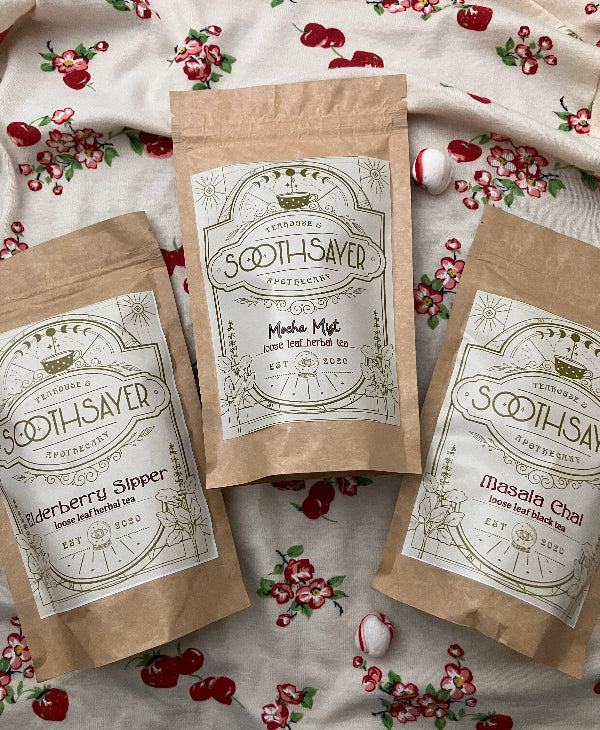 Three packages of 'Soothsayer' tea on a floral fabric background