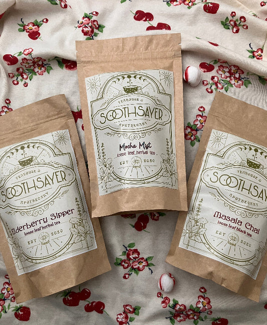 Three packages of 'Soothsayer' tea on a floral fabric background