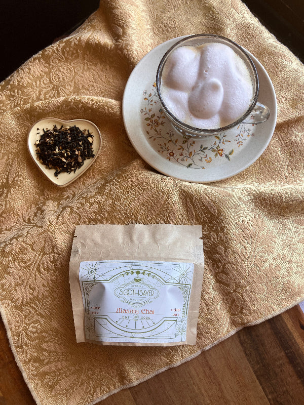 Tea bag, cup of tea with whipped cream, and tea leaves on a textured fabric surface
