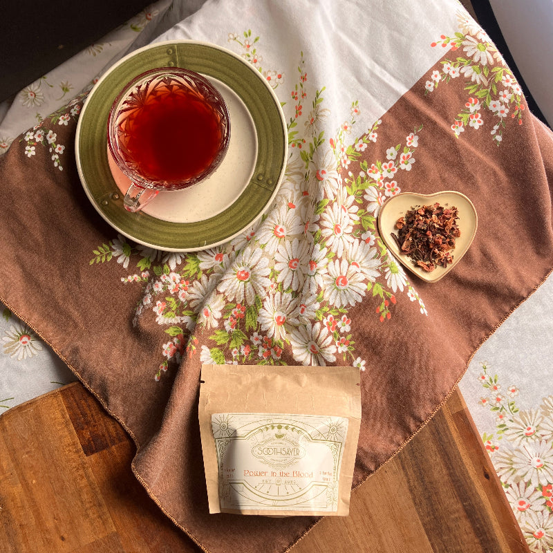Tea cup with a floral pattern on a wooden table with a tea bag and loose tea leaves.